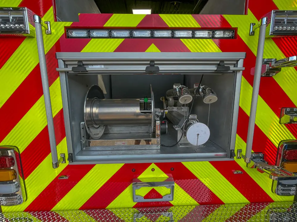 Exterior view of small fire truck showing cab, body compartments, and wheel/tire area.